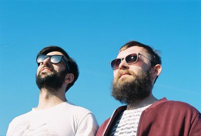 Male friends wearing sunglasses against clear blue sky