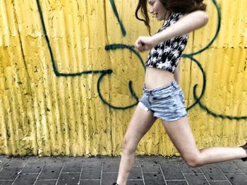 Cheerful woman running on footpath against graffiti on corrugated fence