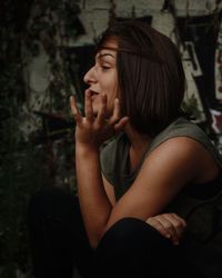 Young woman looking away while sitting against stone wall