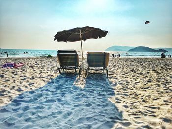 Beach umbrella with deck chairs at beach against sky