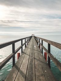 Wooden footbridge over sea against sky