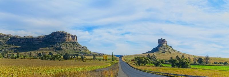 Panoramic shot of road amidst field against sky