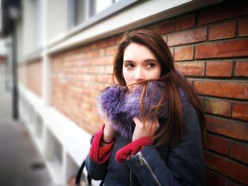 Young woman wearing warm clothing while standing against brick wall