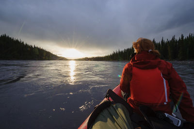 Rear view of man on lake against sky during sunset