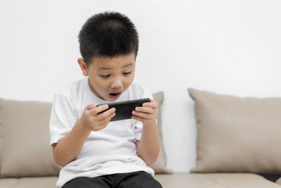 Boy holding mobile phone while sitting on sofa