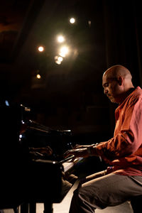 Side view of focus bald male musician playing piano during performance on obscure stage in theater