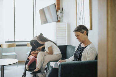 Senior woman reading magazine while sitting on sofa in waiting room