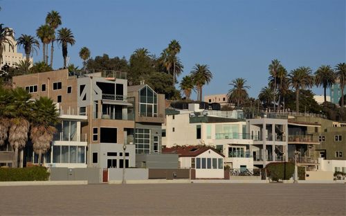 Houses by palm trees and buildings against blue sky