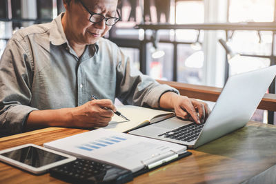 Midsection of businessman using laptop on desk in office