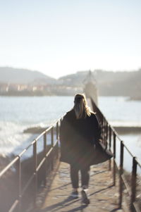 Rear view of woman standing on railing against sky