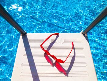 Red sunglasses on the stairs of a pool with turquoise water