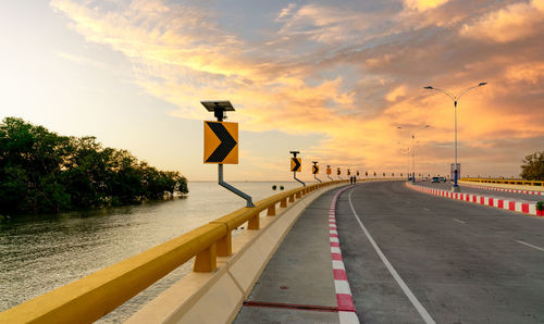 Curve concrete road with curve traffic sign beside the sea at sunset time. solar panel energy.