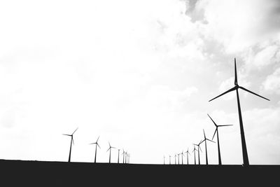 Low angle view of silhouette wind turbines on field against sky