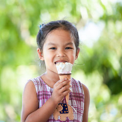 Portrait of cute girl holding ice cream cone while sitting against trees at park