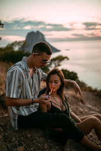 Young woman sitting on shore against sky during sunset