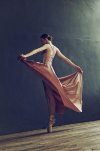 A ballerina in a pink dress and punts moves around the room with a fluttering dress