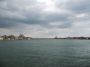 View of buildings by sea against cloudy sky