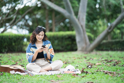 Full length of young woman sitting on grass against trees in forest