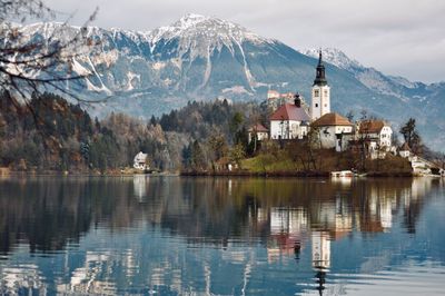 Scenic view of lake by buildings against mountains during winter