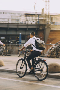 Rare view of male executive riding bicycle on street in city against sky