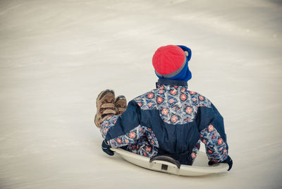 Rear view of boy tobogganing on snow covered field during winter