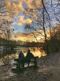 Rear view of silhouette woman sitting by lake against sky during sunset