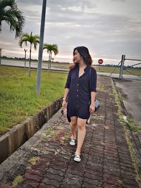 Full length of woman standing on footpath against sky