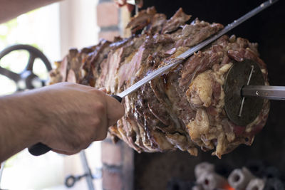 Close-up of man slicing meat from skewer at store