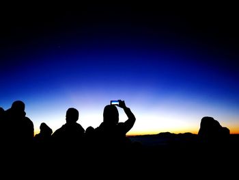 Silhouette people photographing at music concert against clear blue sky