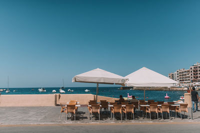 Chairs and tables on beach against clear blue sky