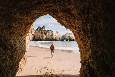 Woman walking at beach seen through cave