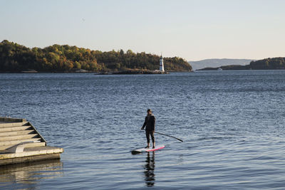 Rear view of man fishing in lake against sky