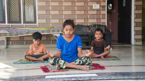 Three indian little kids doing meditate yoga asana on roll mat with eyes closed at home.