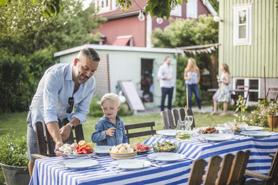 Father talking to son while arranging food plate on table in backyard
