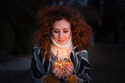 Young woman holding illuminated string lights in jar