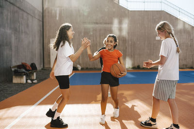 Smiling female friends doing high-five while standing in basketball court