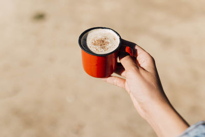 Hand of a woman holding a red enamel cup of coffee with cinnamon and cocoa