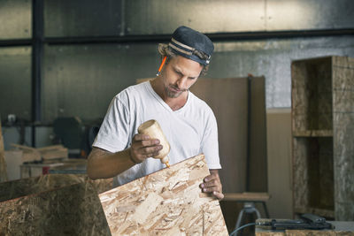 Carpenter applying glue on wooden plank at workshop