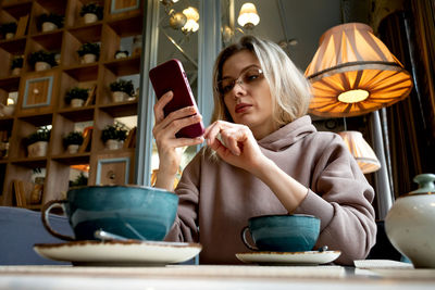 Caucasian middle-aged blonde woman sits in a cafe, drinks coffee and talks on a mobile phone