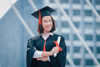 Young woman wearing graduation gown while standing against office building