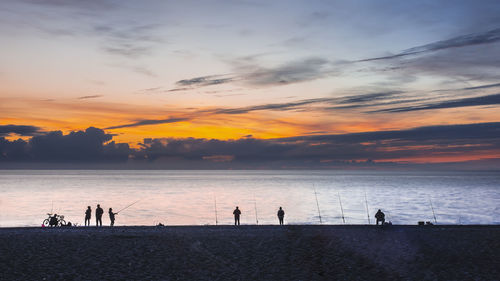 Silhouette people fishing on beach against sky during sunset