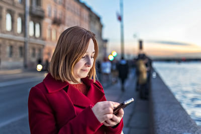  a woman on the embankment of the river in the city, typing text on a smartphone. 