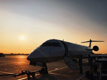 Airplane on airport runway against sky during sunset