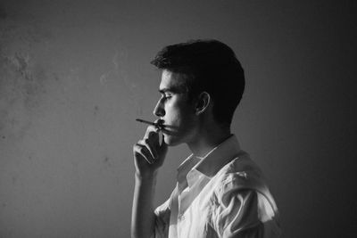 Side view of young man smoking cigarette against gray background