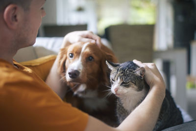 Man sitting on sofa with domestic animals. pet owner stroking his old cat and dog together.