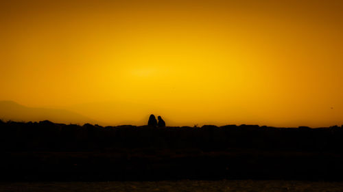 Silhouette people on field against orange sky