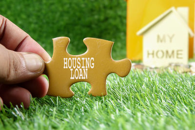 Cropped hand holding jigsaw piece against model house on field