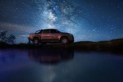 Reflection of car on lake against sky at night