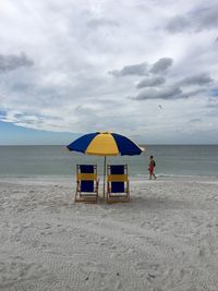 Man walking by parasol at beach against sky