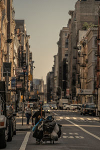 Rear view of man pulling shopping cart with garbage while walking on city street